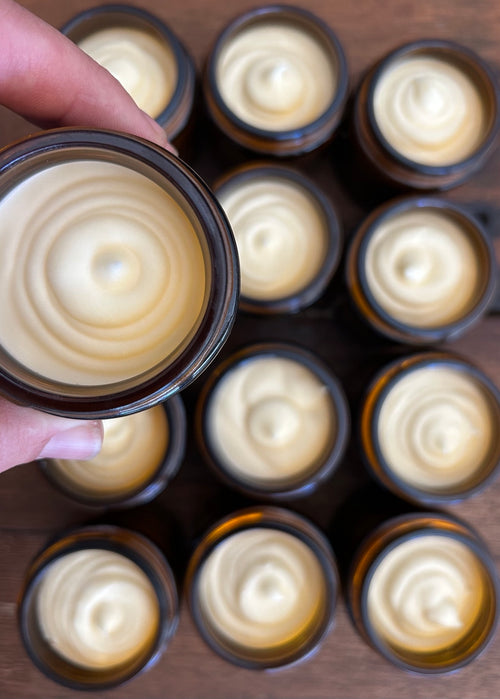 Hand holding an open amber jar of Wentworth Station tallow balm above a batch of jars